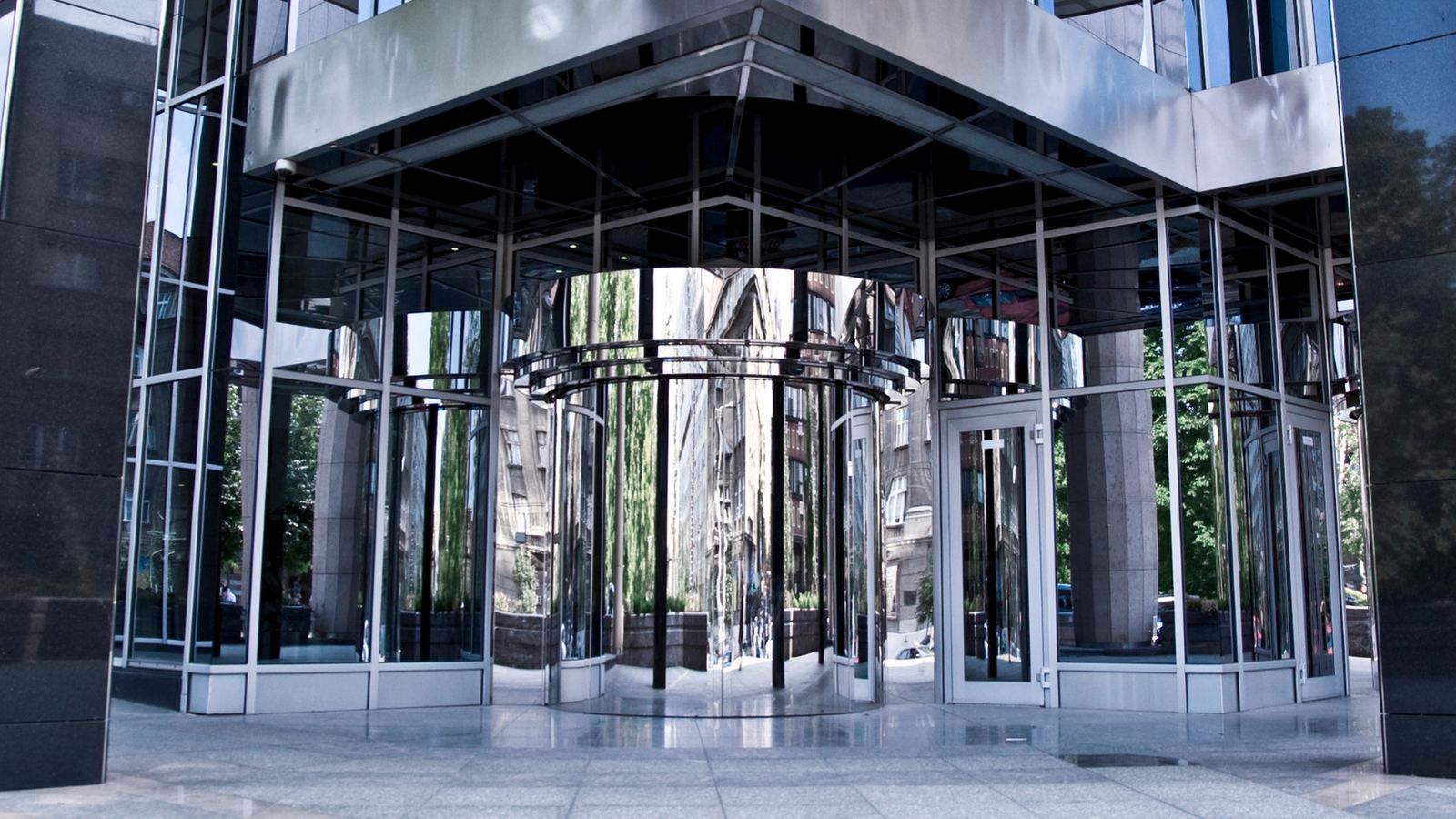 Glass and steel building entrance with a revolving door under a metal canopy